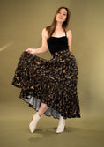 Load image into Gallery viewer, A person wearing a floral maxi skirt with a high-low hem and an adjustable waist, paired with a black top and white boots.