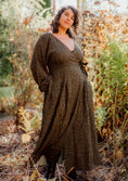 Load image into Gallery viewer, Woman in a long, patterned dress standing in a natural setting with trees and foliage.