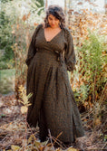 Load image into Gallery viewer, Woman in a long, patterned dress standing in a natural setting with greenery.