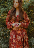 Load image into Gallery viewer, Woman in a patterned dress holding a pomegranate against a natural background