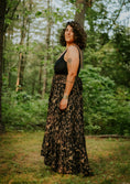 Load image into Gallery viewer, Woman in a black dress with a floral pattern standing in a forest