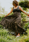 Load image into Gallery viewer, Woman in a black tank top and patterned skirt standing in a garden