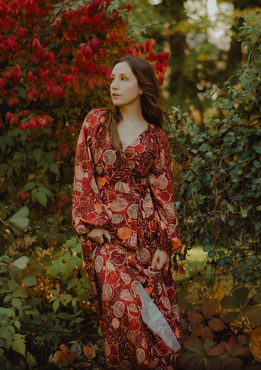 Woman in a red floral dress standing among greenery