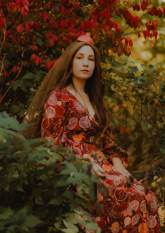 Woman in a red floral dress sitting among autumn foliage