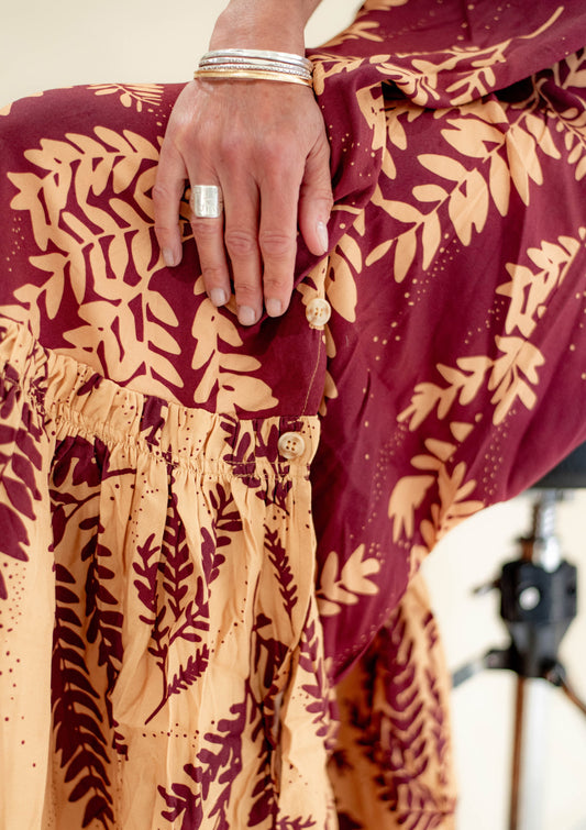 Close-up of a hand wearing a ring on a maroon fabric with leaf pattern